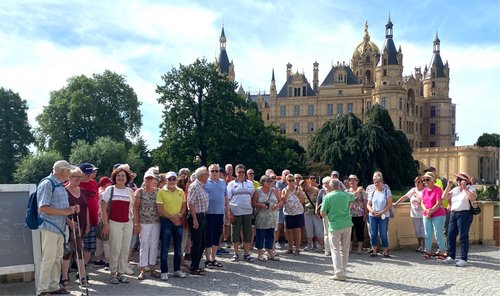 Das Foto zeigt die Reisegruppe der KAB vor dem Schweriner Schloss. Mit dem Rücken zur Kamera in grünem Shirt der Reiseführer Dr. Horn.